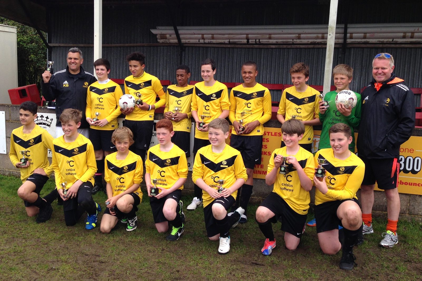 Celsius Software sponsored youth football team in branded yellow kit holding trophies with their coaches